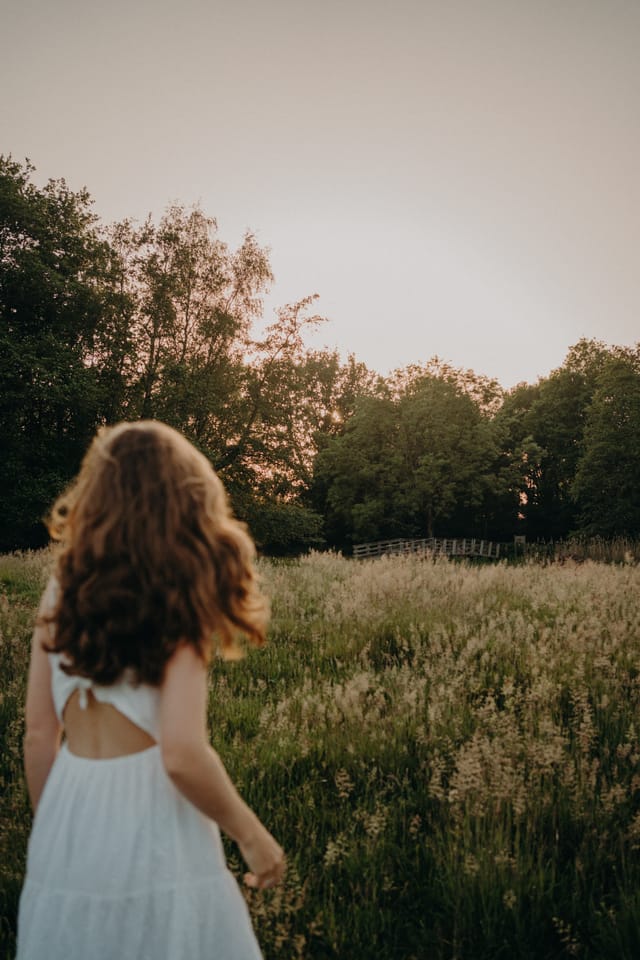 Vrouw van achteren lopend in een veld bij zonsondergang