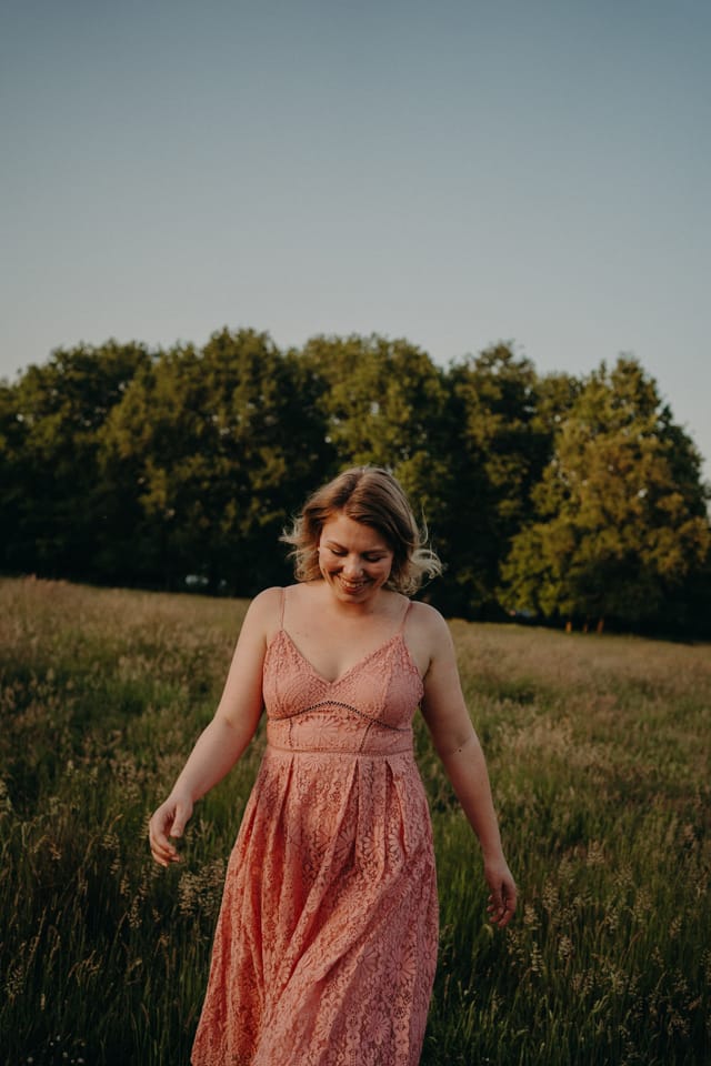 Vrouw in roze kanten jurk in een veld bij gouden uur